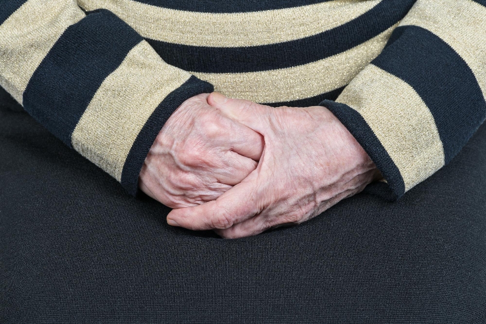 Elderly hands clasped together, resting in a striped sweater lap.